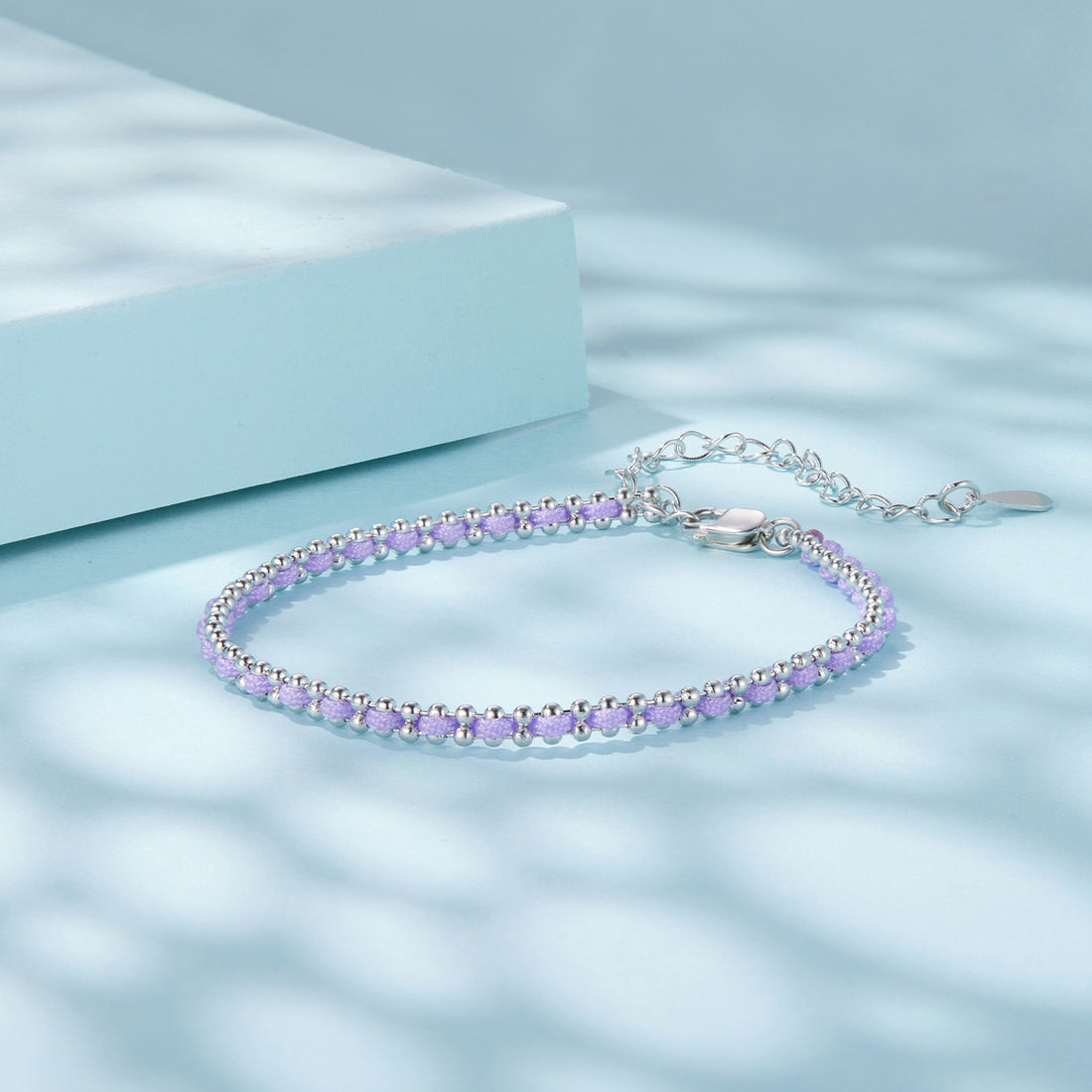 Silver bracelet with purple beads on a light blue background