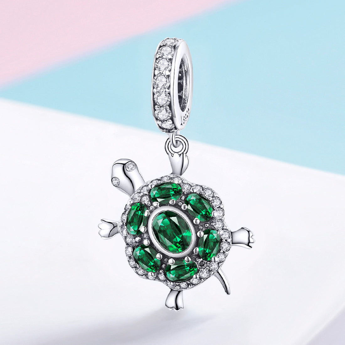 Tortoise-shaped pendant with green gemstones on a light background