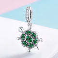 Tortoise-shaped pendant with green gemstones on a light background