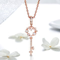 Rose gold key-shaped pendant necklace with heart details on a white background