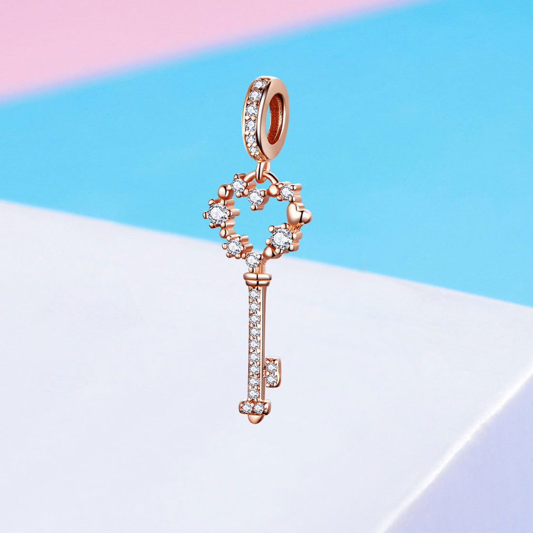 Rose gold key-shaped pendant with diamonds on a pastel background