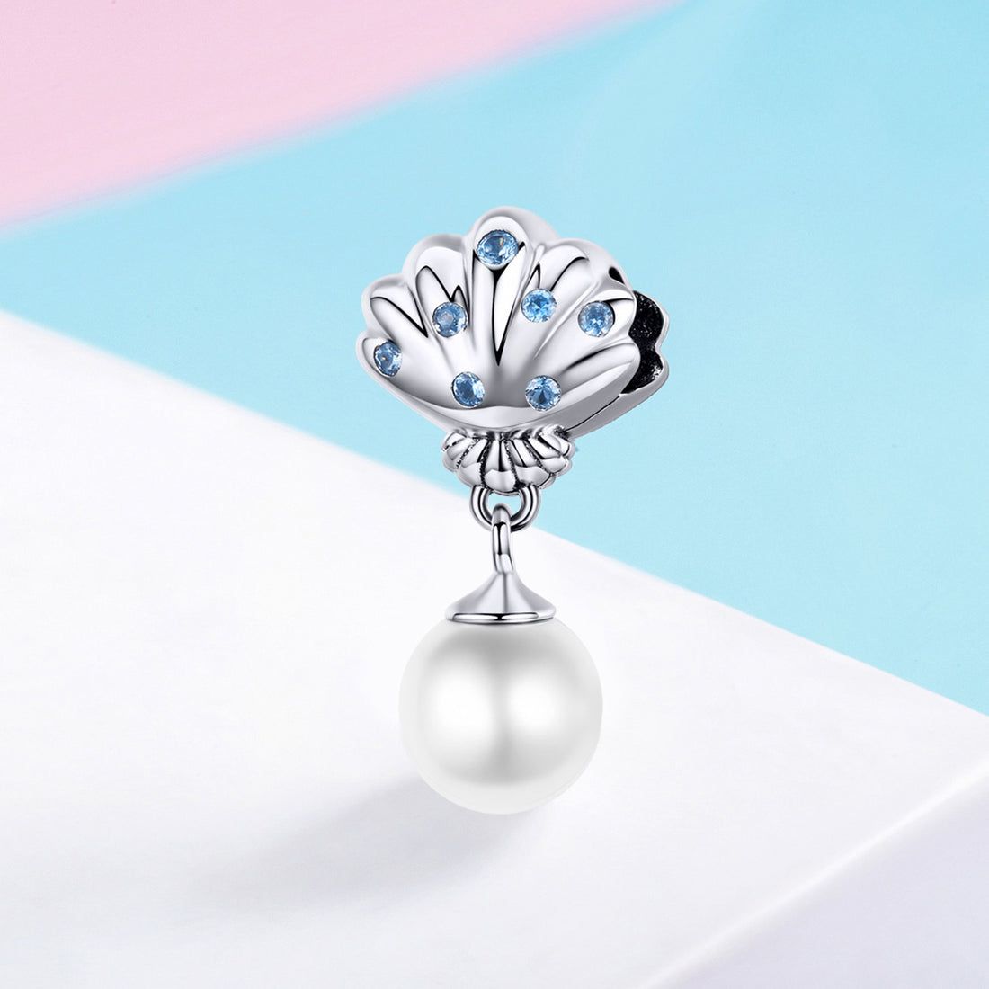 Pearl charm with shell design and blue stones on a colorful background