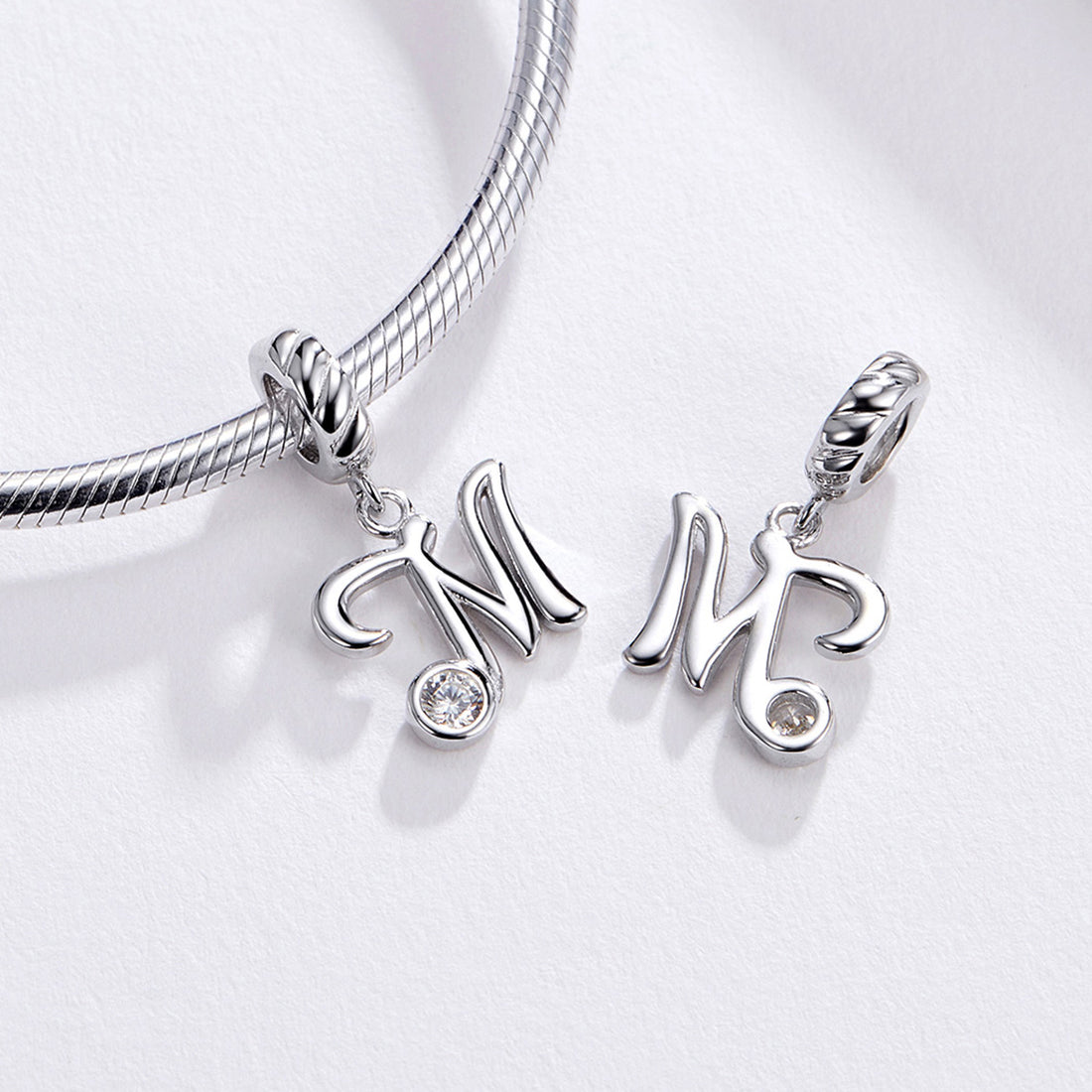 Silver pendant with letter 'M' and clear gemstone on a white background
