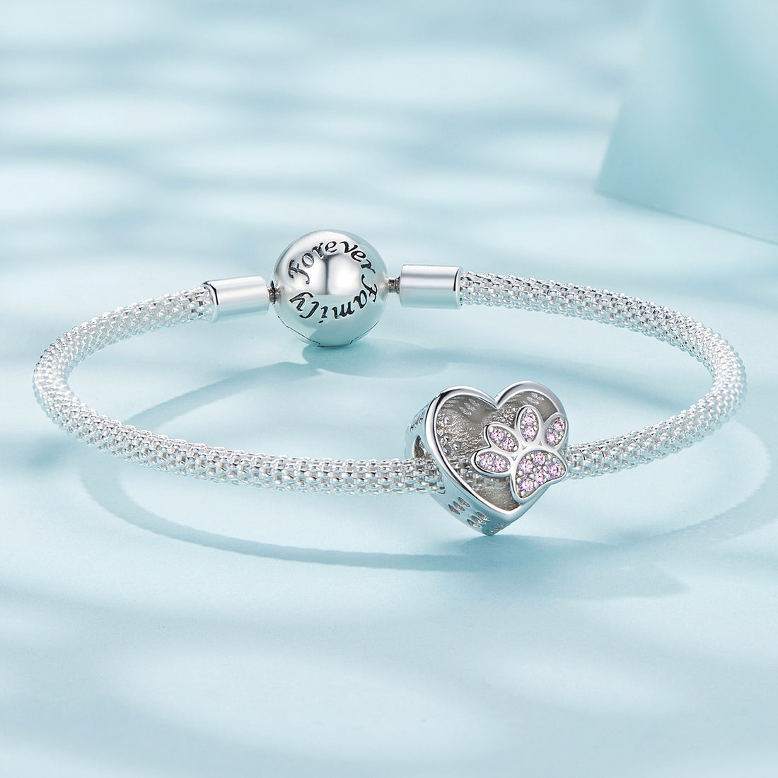 Heart-shaped charm with paw prints and pink stones on a light blue background