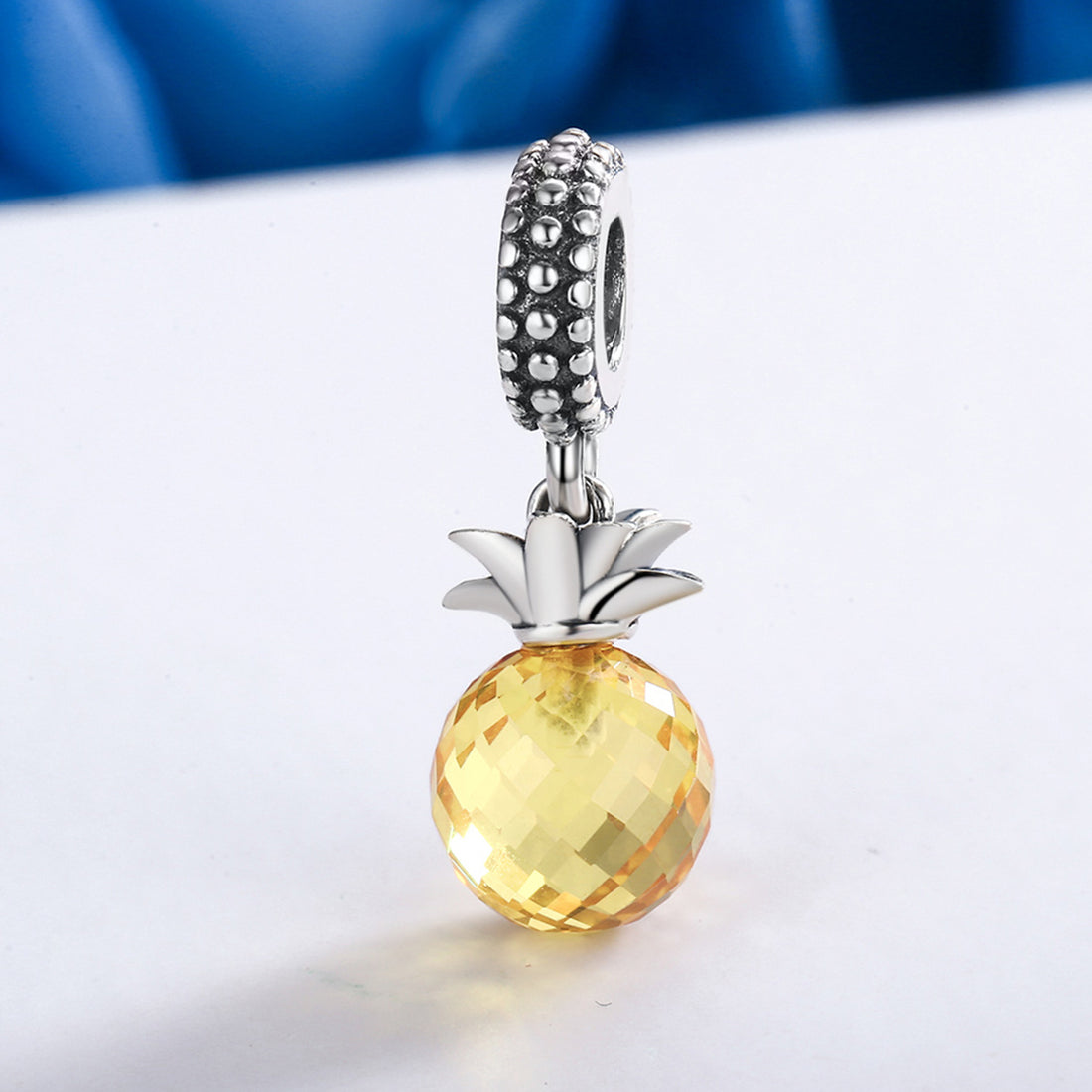 Pineapple-shaped charm with yellow center and silver top on a white background