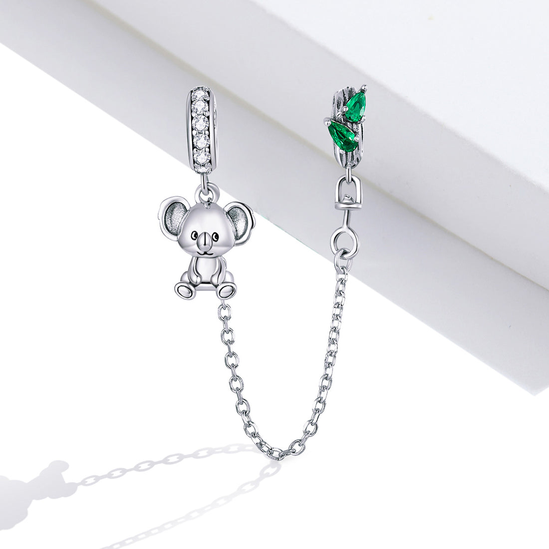 Silver teddy bear charm with a chain and green gemstone on a white background