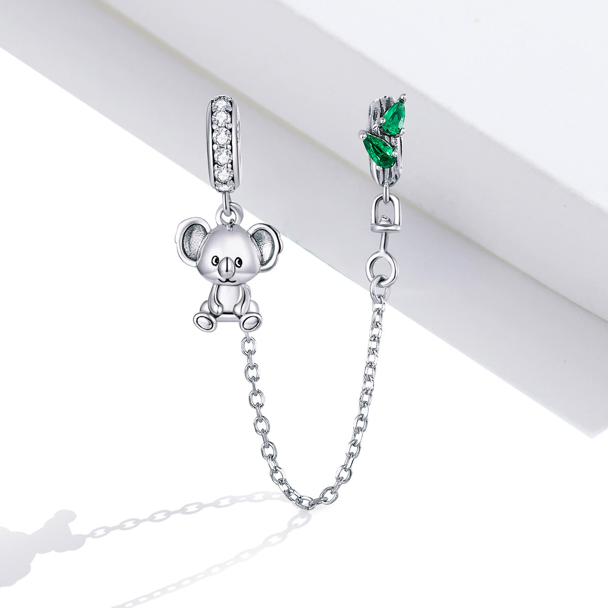 Silver teddy bear charm with a chain and green gemstone on a white background