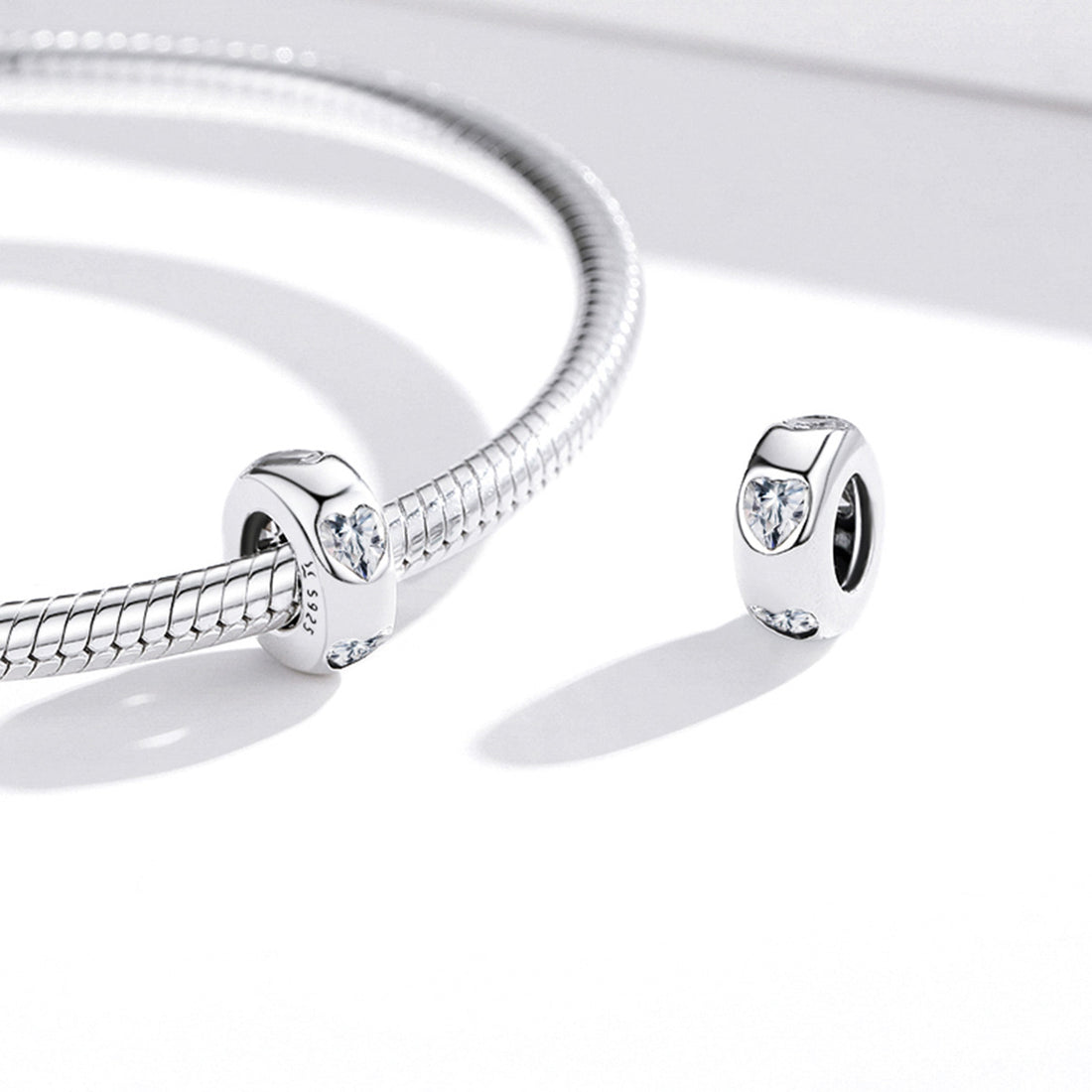 Silver charm with heart-shaped and round cut gemstones on a white background