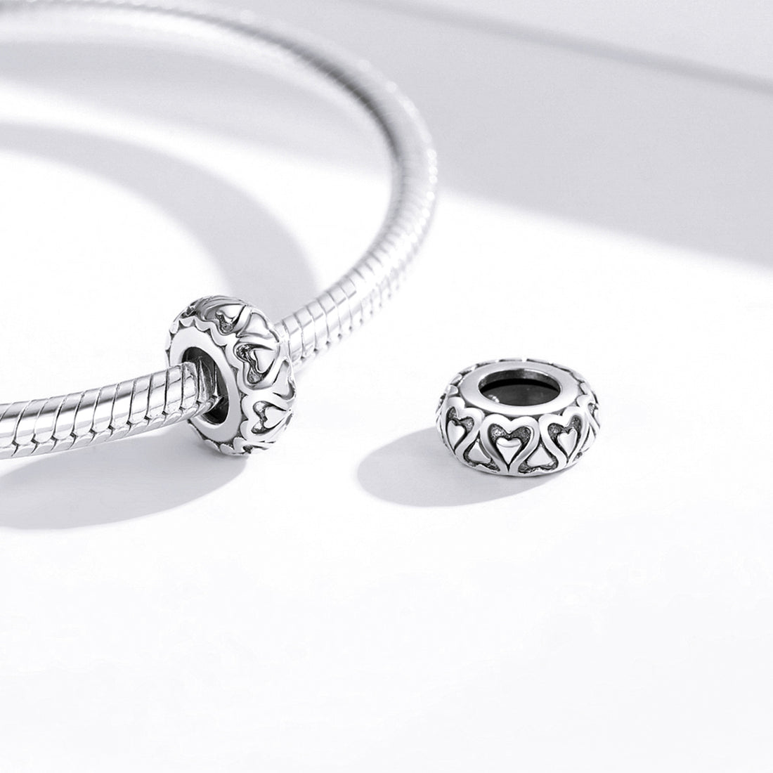 Silver jewelry charm with intricate heart design on a white background