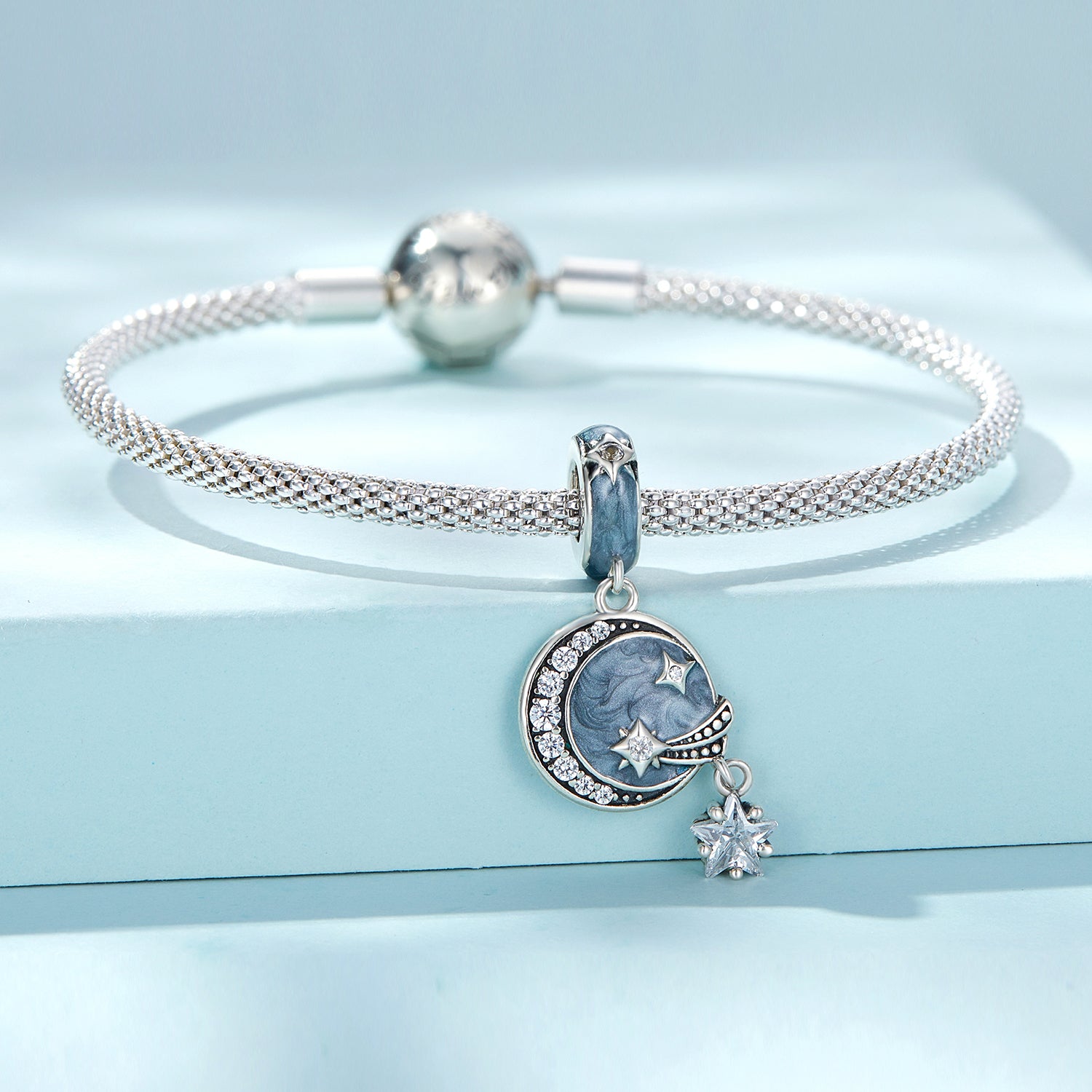 Silver bracelet with a moon and star charm on a light blue background
