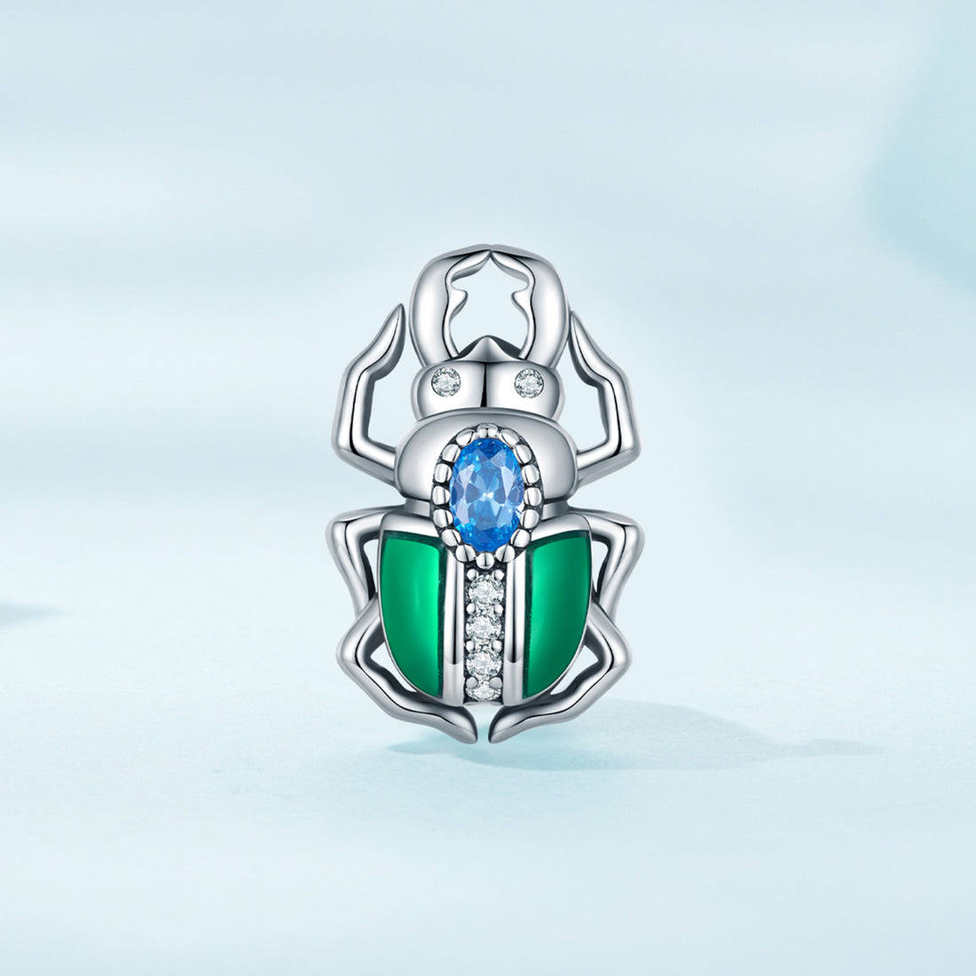 Silver beetle-shaped pendant with green and blue gemstones on a light blue background