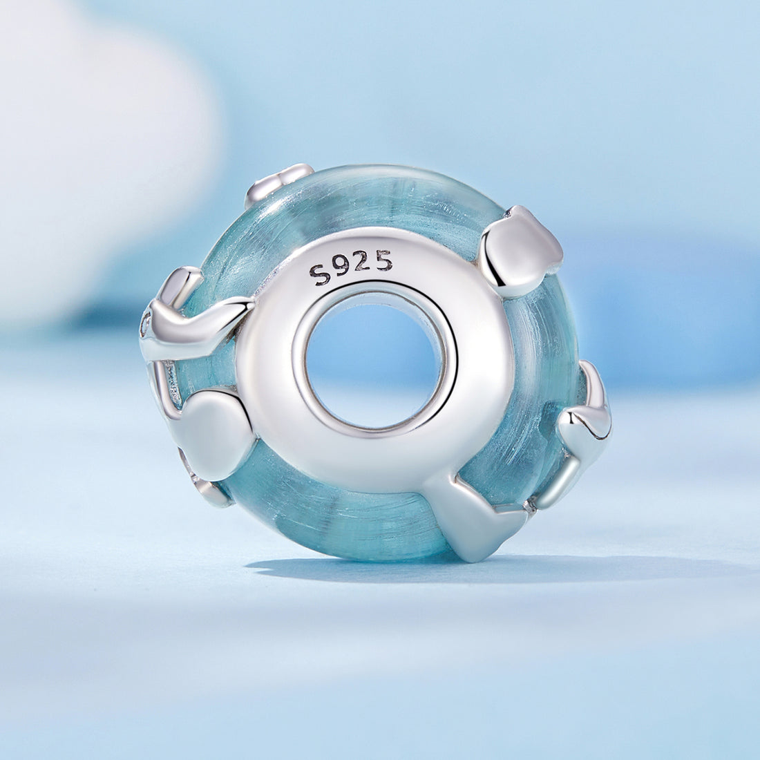 Silver charm with blue glass bead on a light blue background