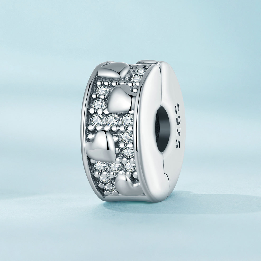 Silver charm with heart design and '925' stamp on a light blue background