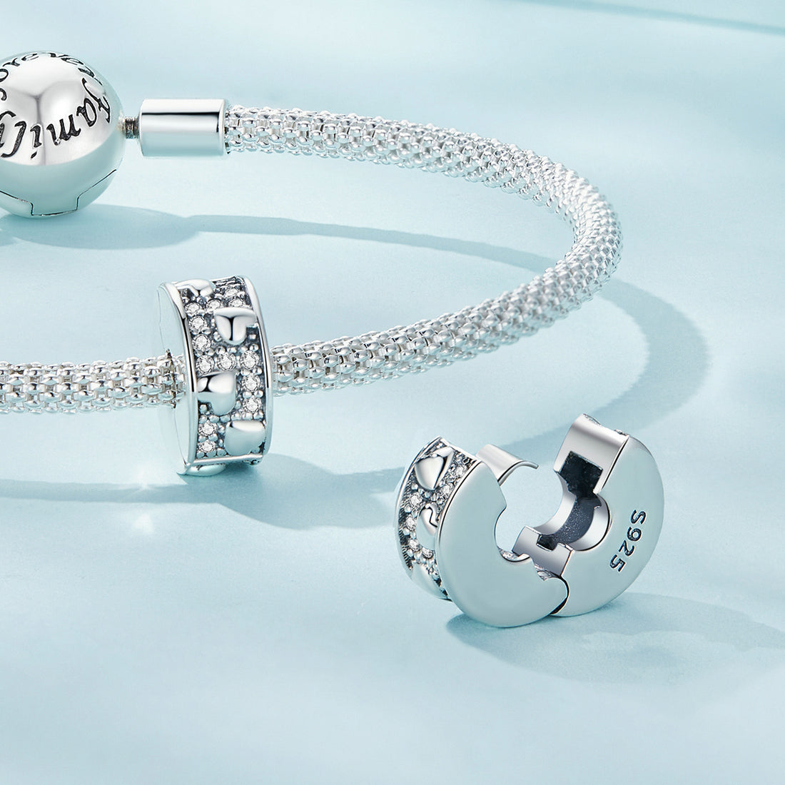 Silver charm with heart design and '925' stamp on a light blue background