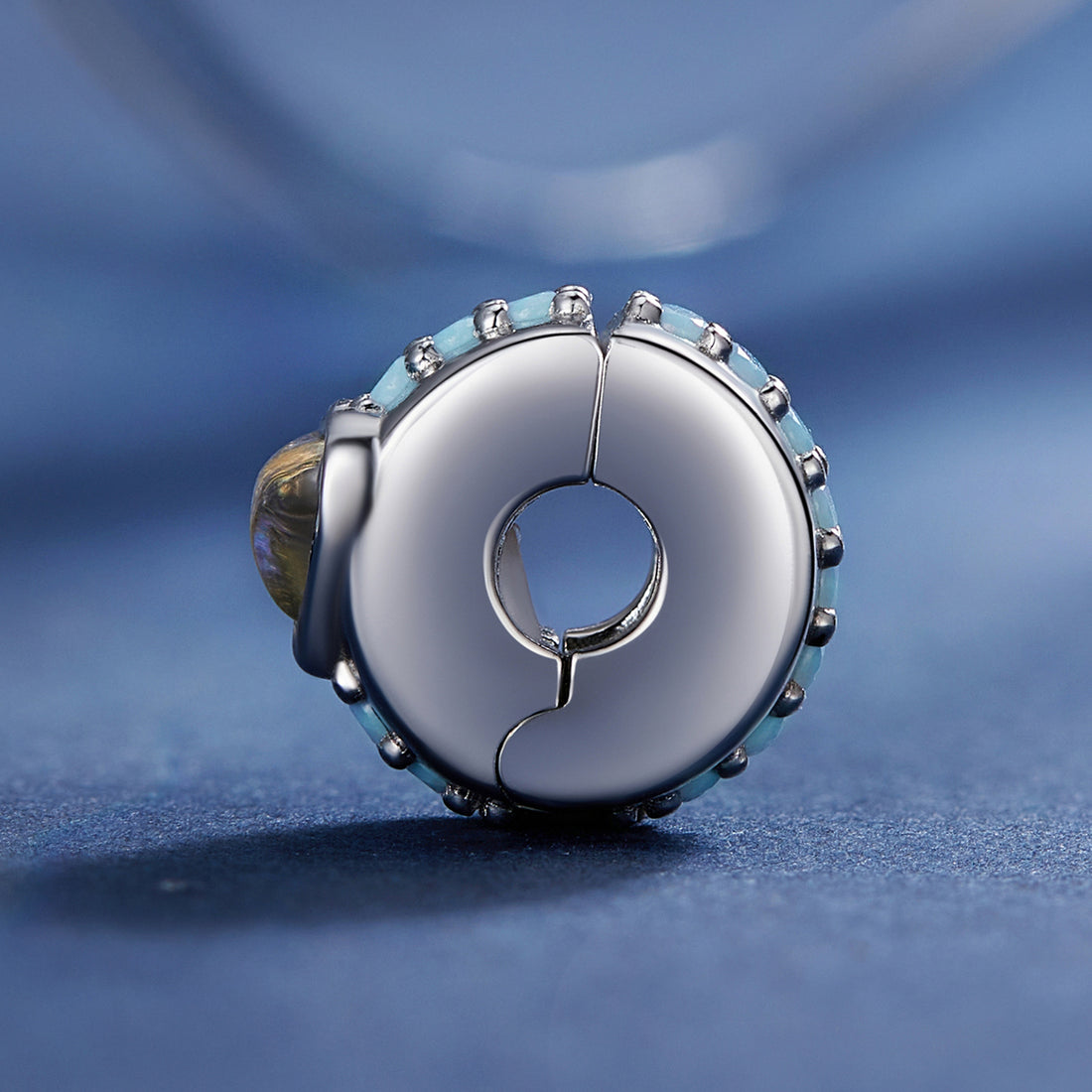 Silver charm with a blue heart-shaped gem on a blue background
