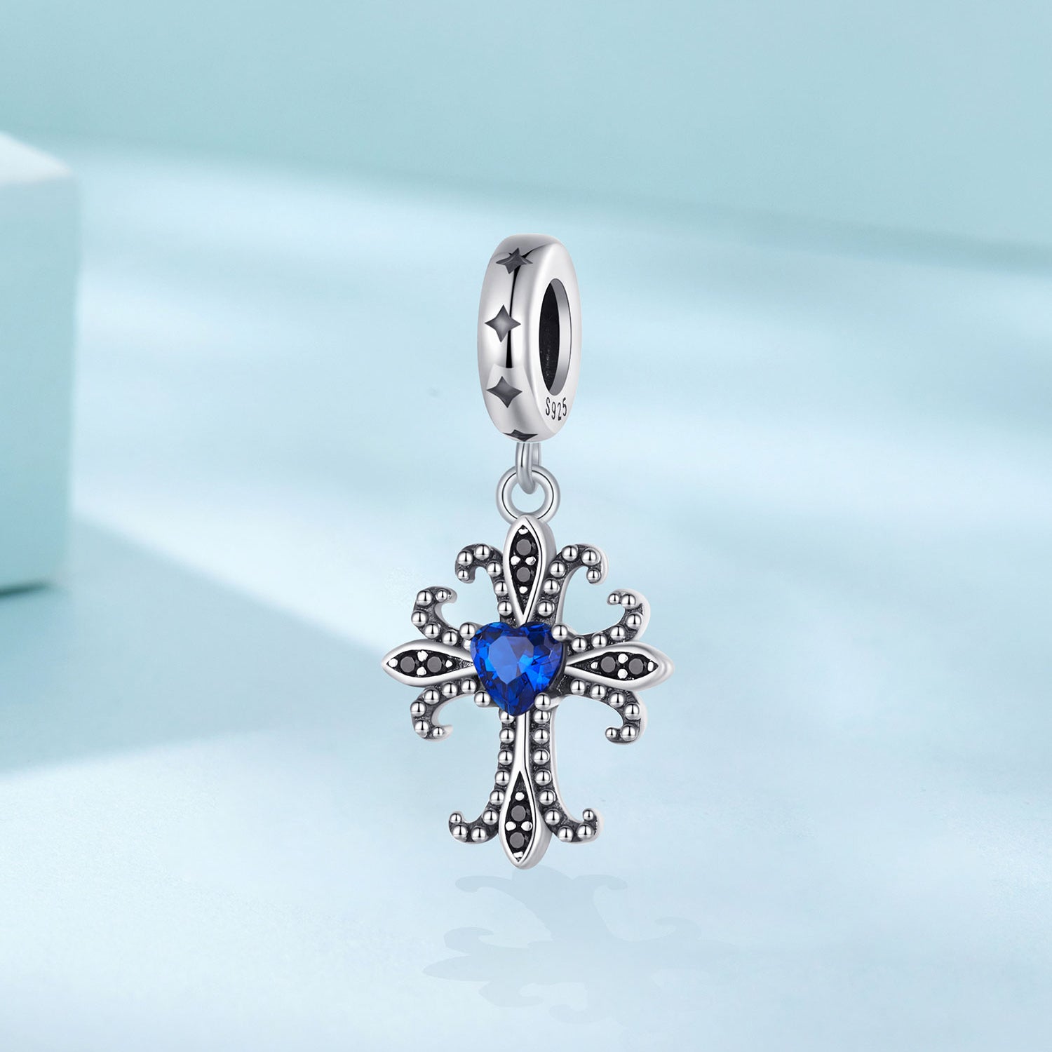 Silver cross-shaped pendant with a blue gemstone on a light blue background