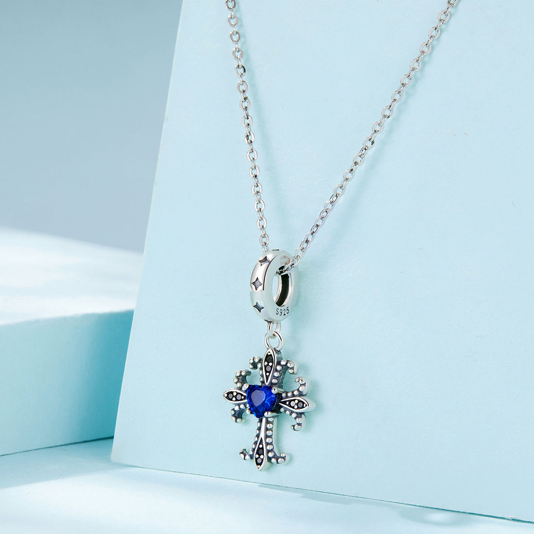 Silver cross-shaped pendant with a blue gemstone on a light blue background