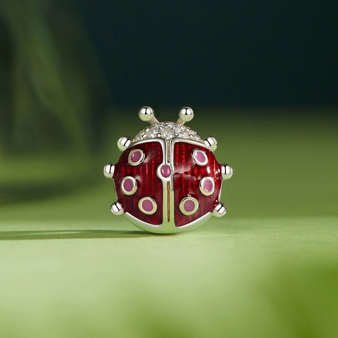 Red and silver ladybug-shaped jewelry charm on a green background