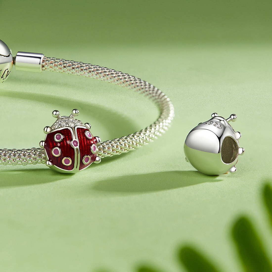 Red and silver ladybug-shaped jewelry charm on a green background