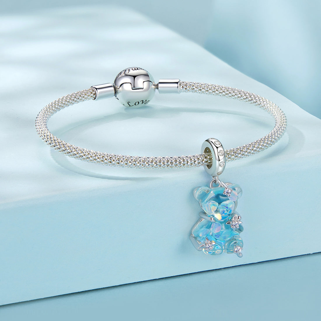 Silver bracelet with a blue teddy bear charm on a light blue background