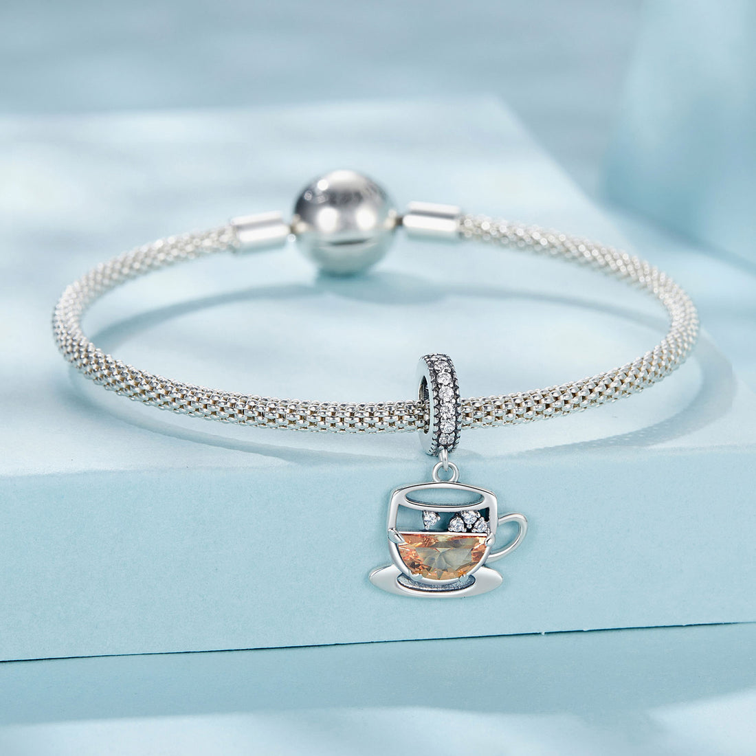 Silver teacup charm with gemstones on a light blue background