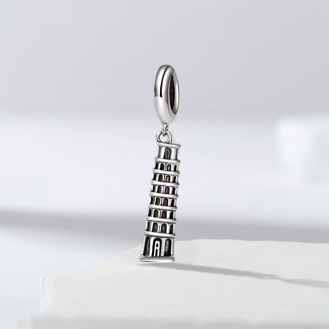 Silver charm shaped like the Leaning Tower of Pisa on a light gray background