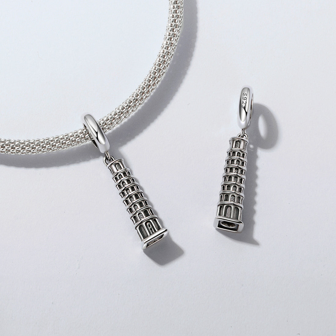 Silver charm shaped like the Leaning Tower of Pisa on a light gray background