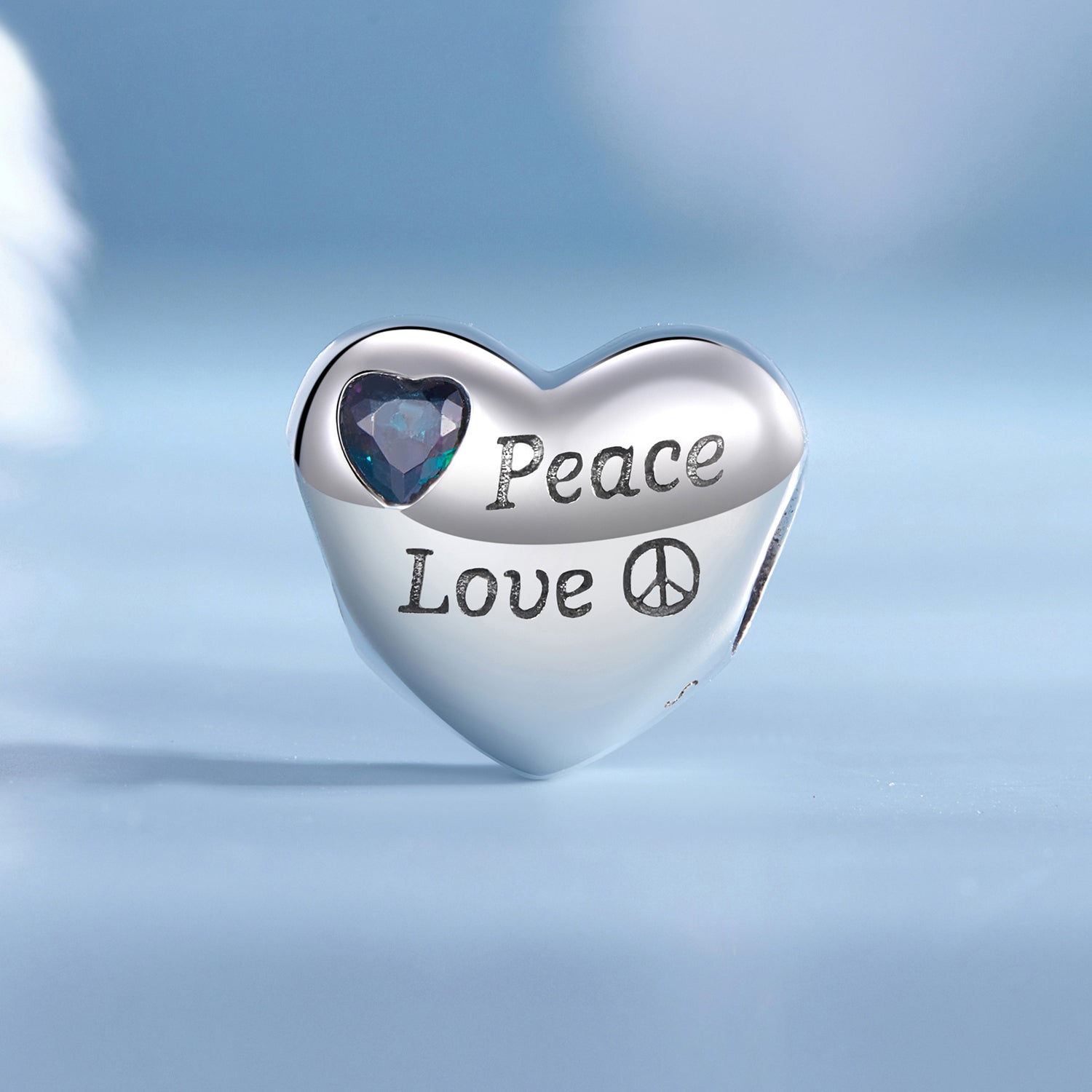 Heart-shaped silver charm with 'Peace Love' engraving on a light blue background