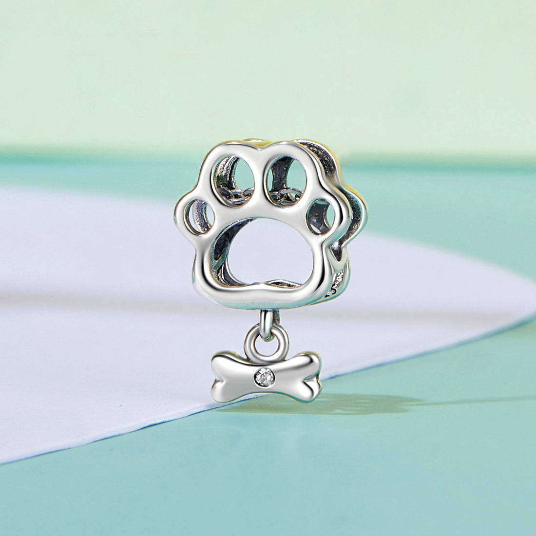 Silver paw print charm with a bone pendant on a pastel background