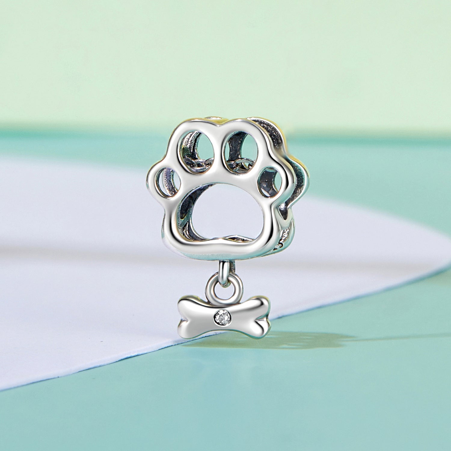 Silver paw print charm with a bone pendant on a pastel background