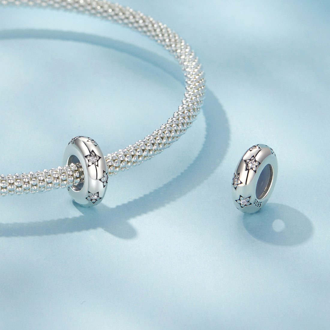 Silver bracelet with two matching charms on a light blue background