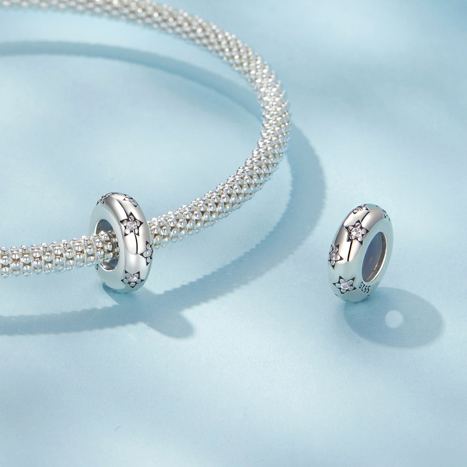Silver bracelet with two matching charms on a light blue background