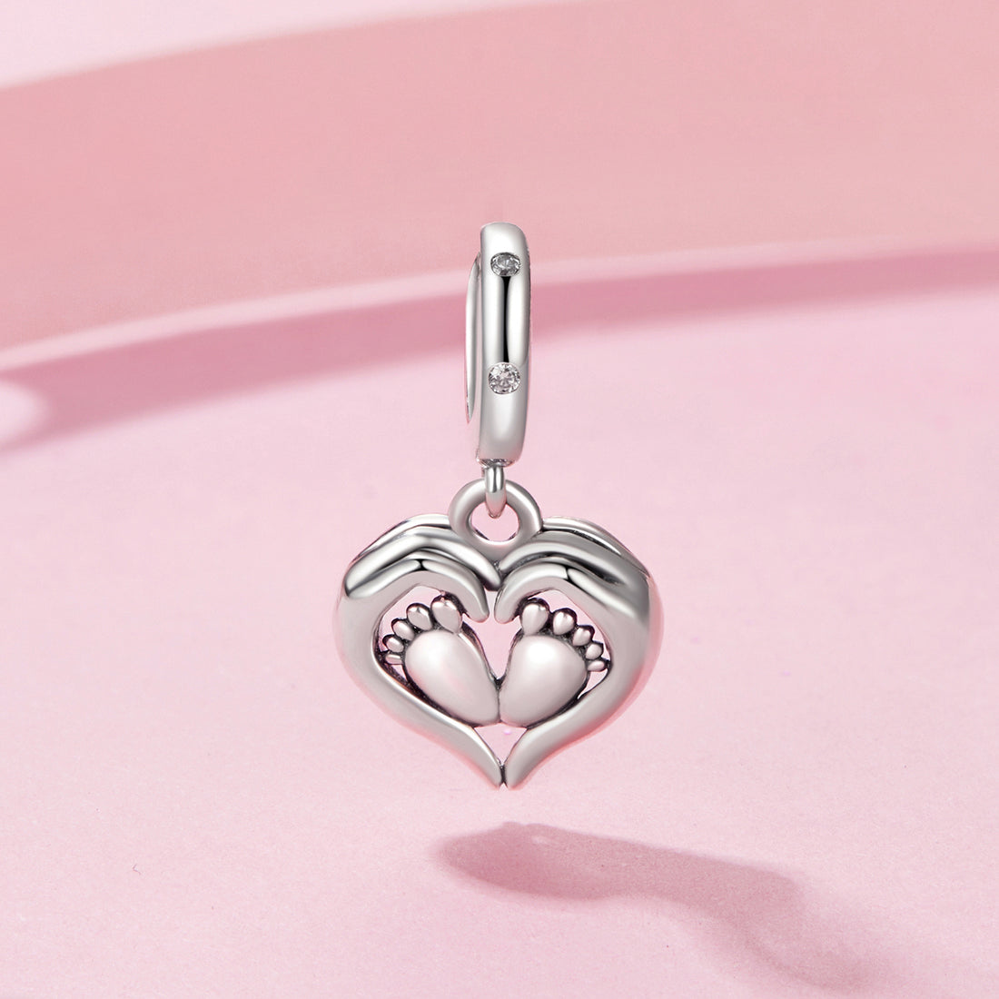 Silver charm with heart design and footprints on a pink background