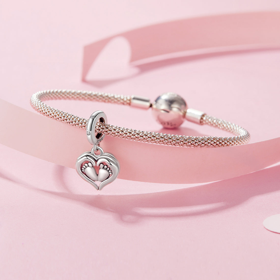 Silver charm with heart design and footprints on a pink background