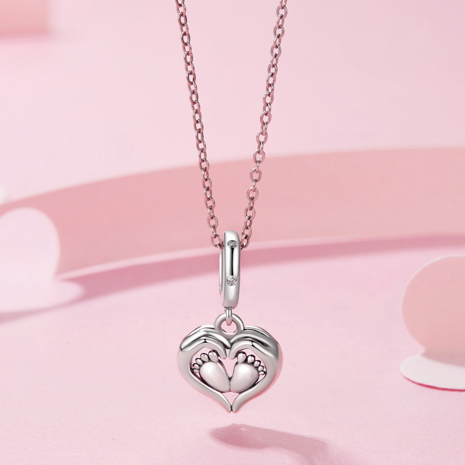 Silver heart-shaped necklace with footprints on a pink background