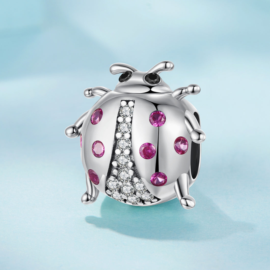 Silver ladybug charm with pink gemstones on a light blue background
