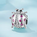 Silver ladybug charm with pink gemstones on a light blue background