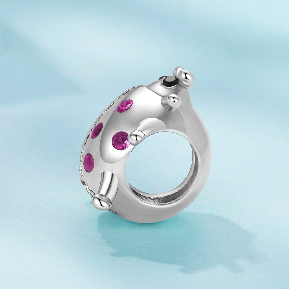Silver ladybug charm with pink gemstones on a light blue background