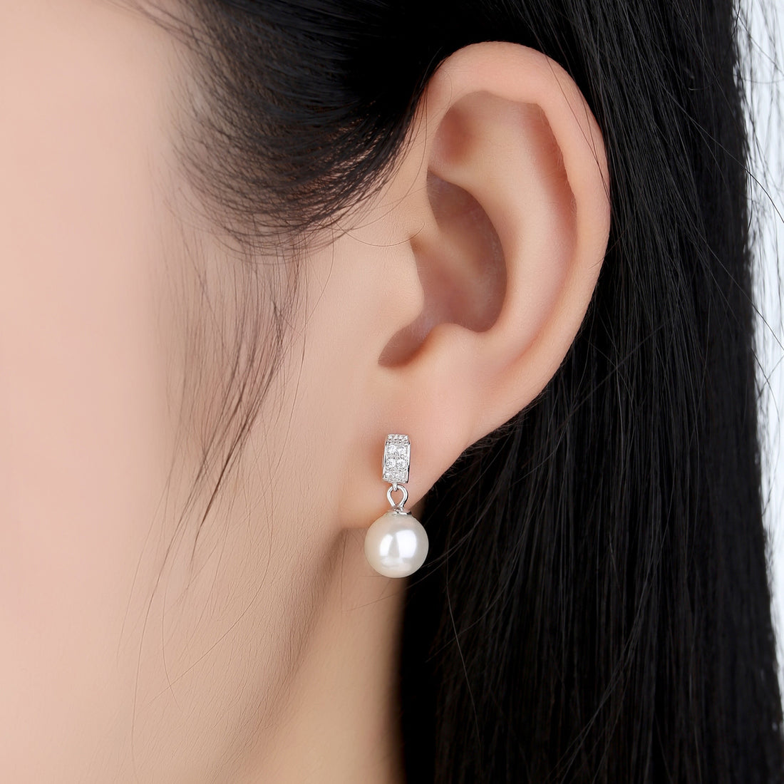 Pearl earrings with diamond accents on a light gray background