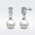Pearl earrings with diamond accents on a light gray background