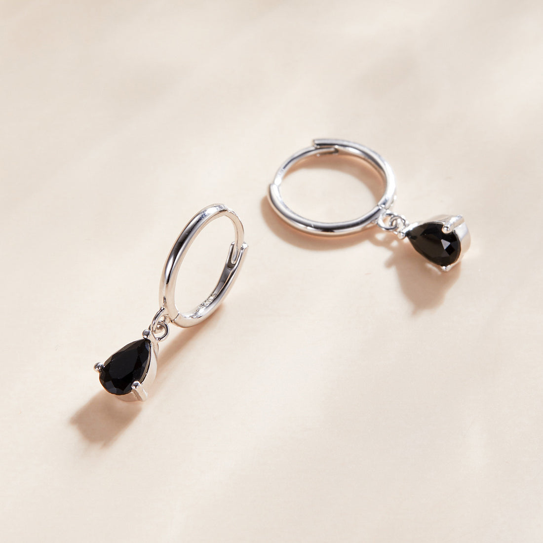 Silver hoop earrings with black teardrop gemstones on a white background