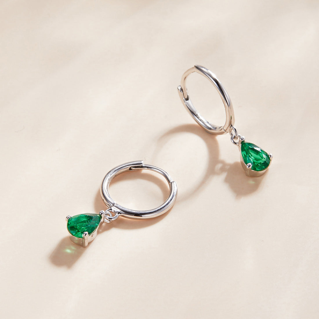 Silver hoop earrings with green gemstones on a beige background