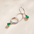 Silver hoop earrings with green gemstones on a beige background