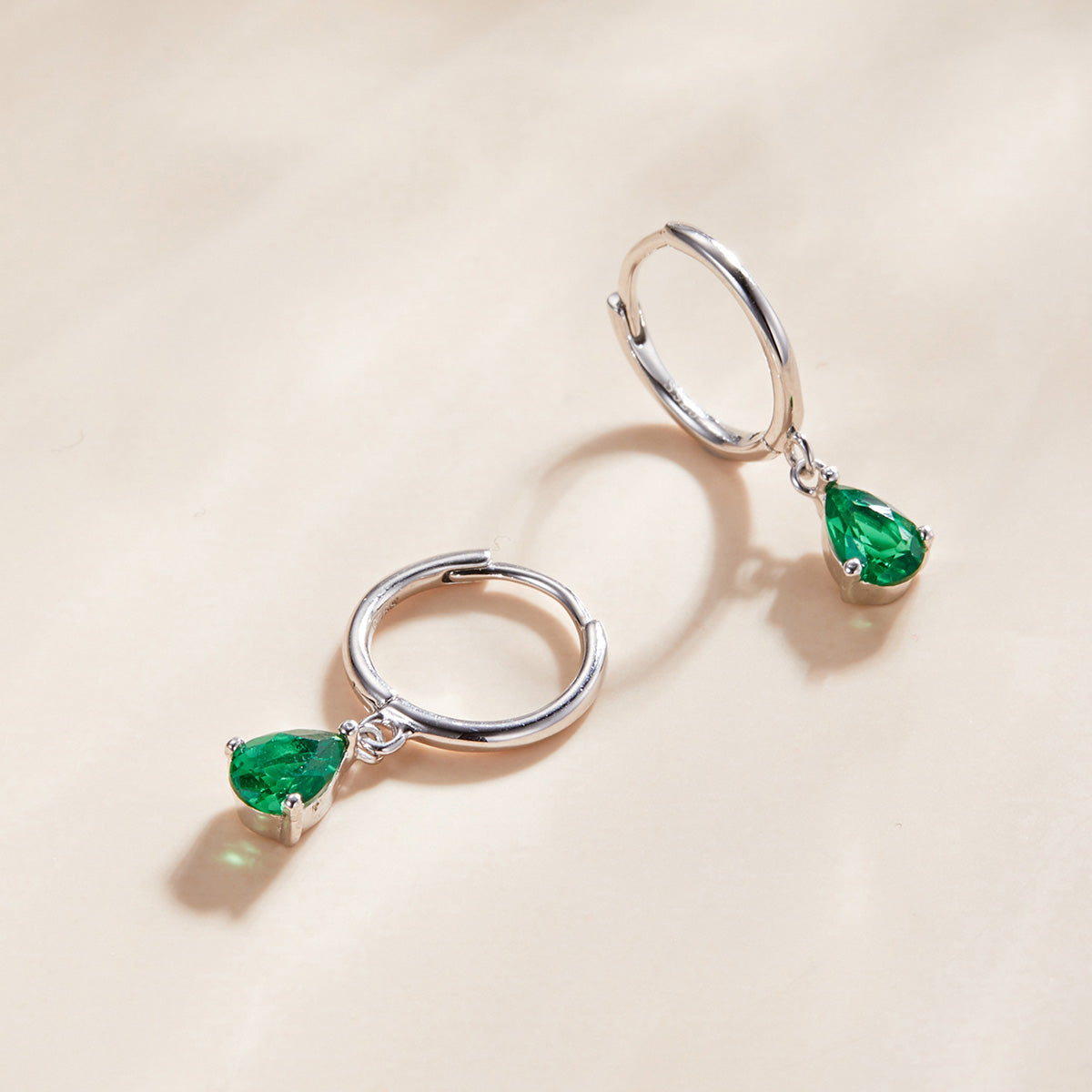 Silver hoop earrings with green gemstones on a beige background