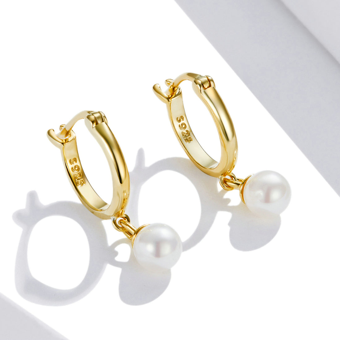 Gold hoop earrings with pearl drops on a white background