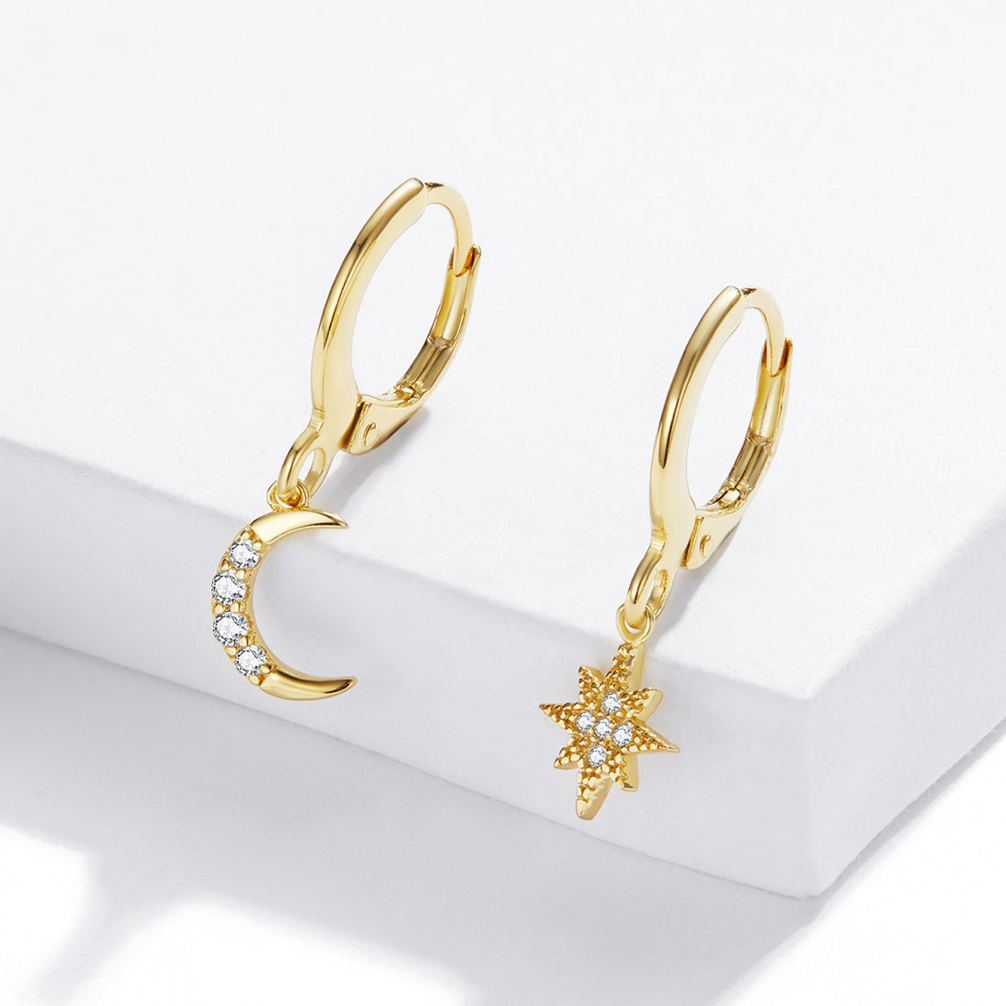 Gold hoop earrings with moon and star charms on a white surface