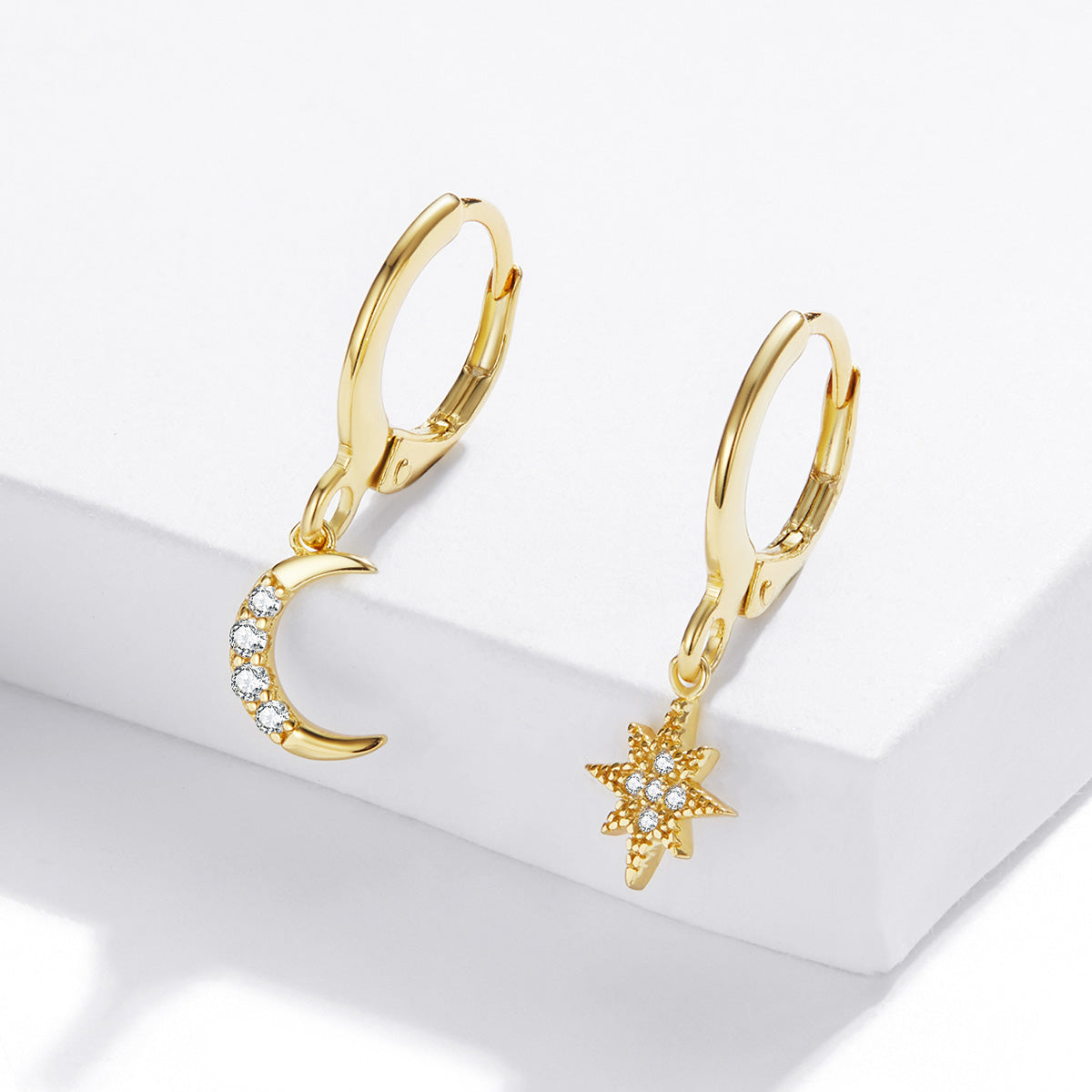 Gold hoop earrings with moon and star charms on a white surface