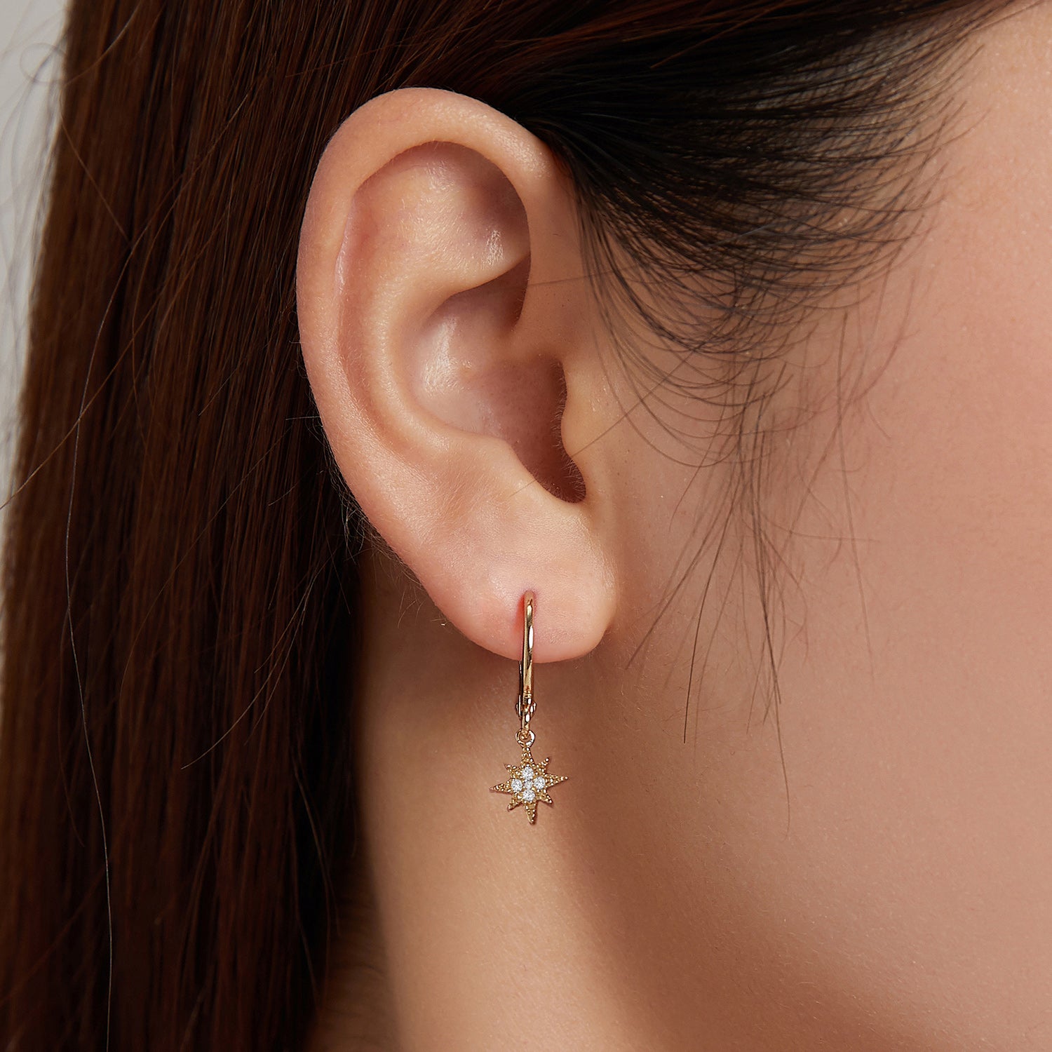Close-up of an ear wearing a gold earring with a star design.