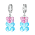 Gummy bear-shaped earrings with blue bodies and pink cheeks on a white background
