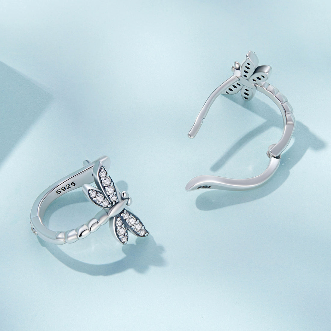 Silver dragonfly-shaped earrings with clear gemstones on a white background